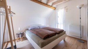 Et soveværelse med skråvæg, en seng med to puder, en radiator og en lille skammel.