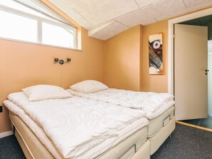 Un lit double avec une literie blanche, dans une pièce aux murs de couleur beige et dotée d’une fenêtre.