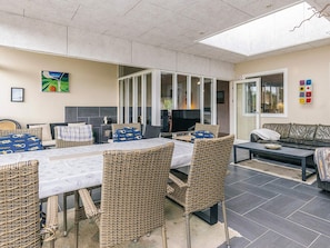 Amplo espaço interno com mesa de jantar, cadeiras de vime, sofá e televisão.