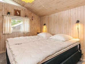 A wooden-paneled bedroom with a bed, two bedside lamps, a window with curtains, and a small shelf with a plant. - 10 Person Holiday Home in Storvorde (Storvorde)