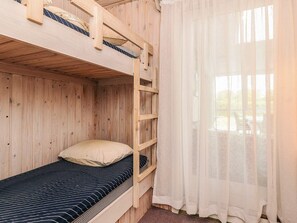 A wooden bunk bed room with a window and sheer curtains.