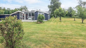 Et moderne hus med stor glasfacade, overdækket terrasse og velplejet græsplæne.