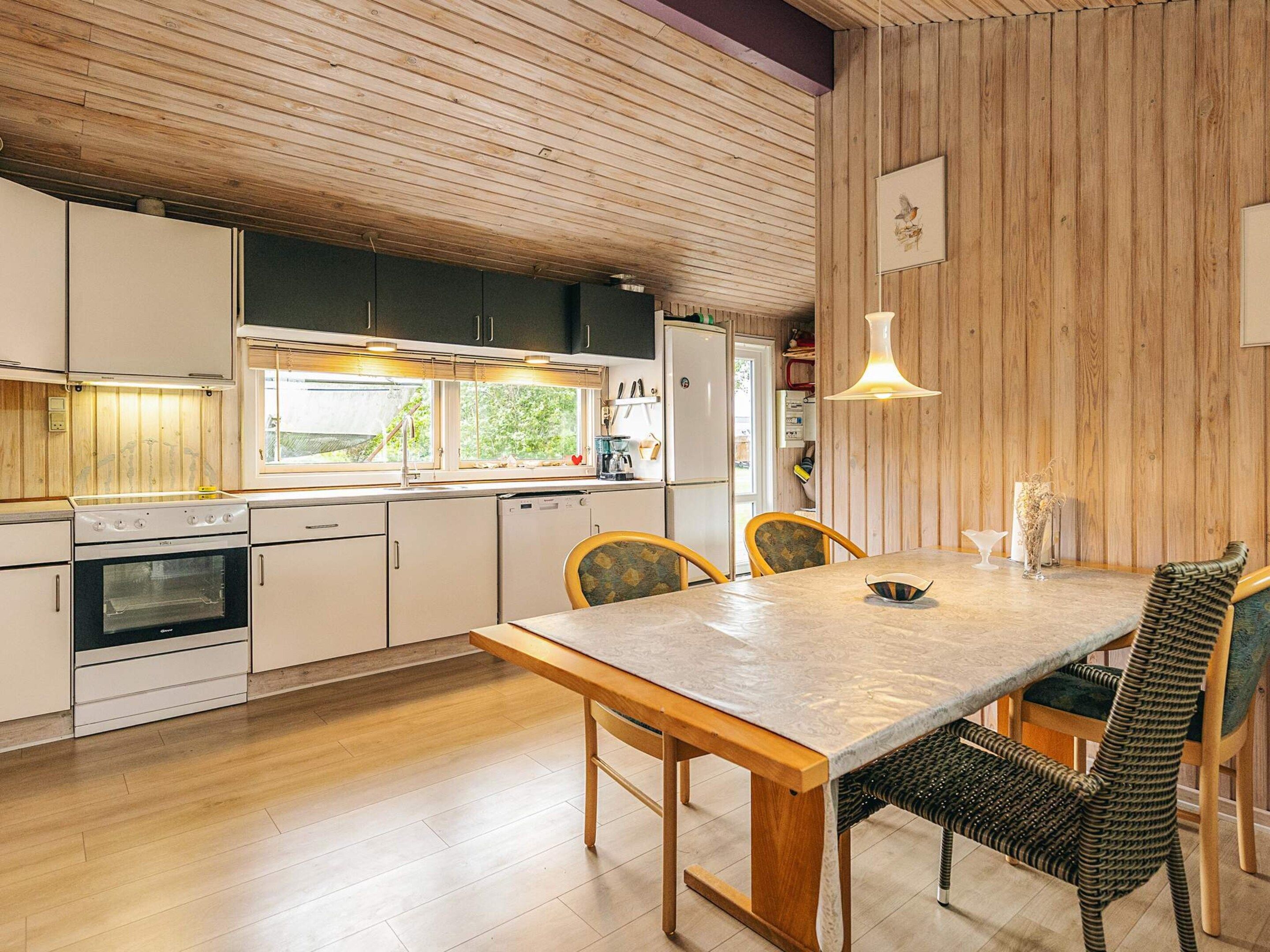 A modern kitchen with wooden cabinets, a dining table with chairs, and a hanging light fixture.