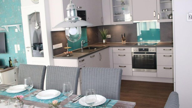 Una cocina moderna con armarios blancos, un horno de acero inoxidable y un comedor con una mesa dispuesta para cuatro personas.