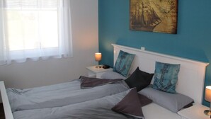 Un dormitorio con dos camas, una ventana con cortinas traslúcidas, un cuadro en la pared y lámparas de noche.