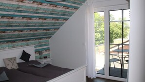 Un dormitorio con techo inclinado, una cama, una mesita de noche y vistas a un patio exterior con mesa y sillas.