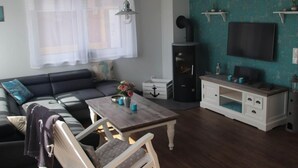 Una sala de estar con un sofá de color oscuro, una mesa de centro de madera, un sillón blanco, un televisor montado en la pared y una chimenea.
