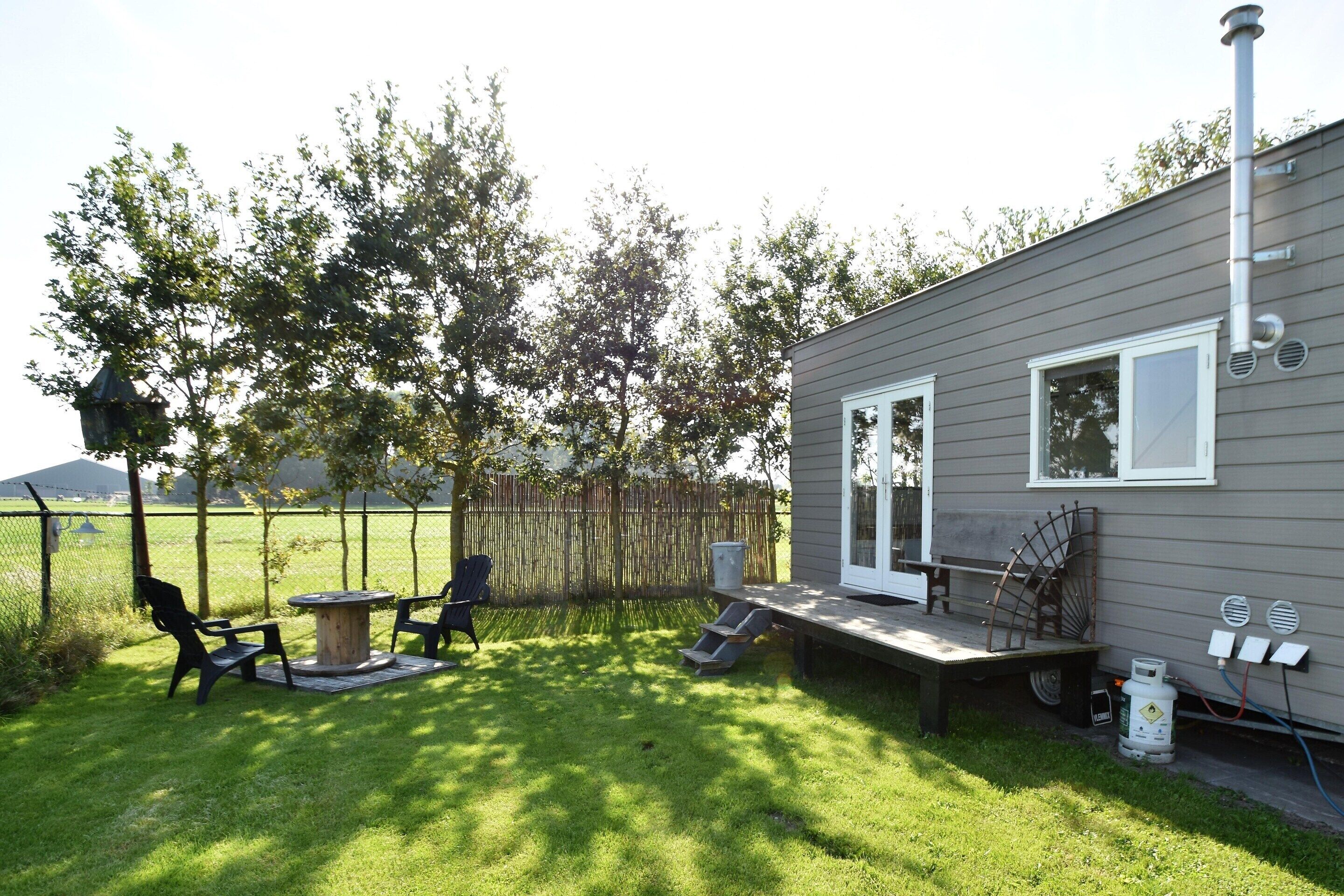 Une petite maison avec une terrasse, une table et deux chaises dans le jardin.