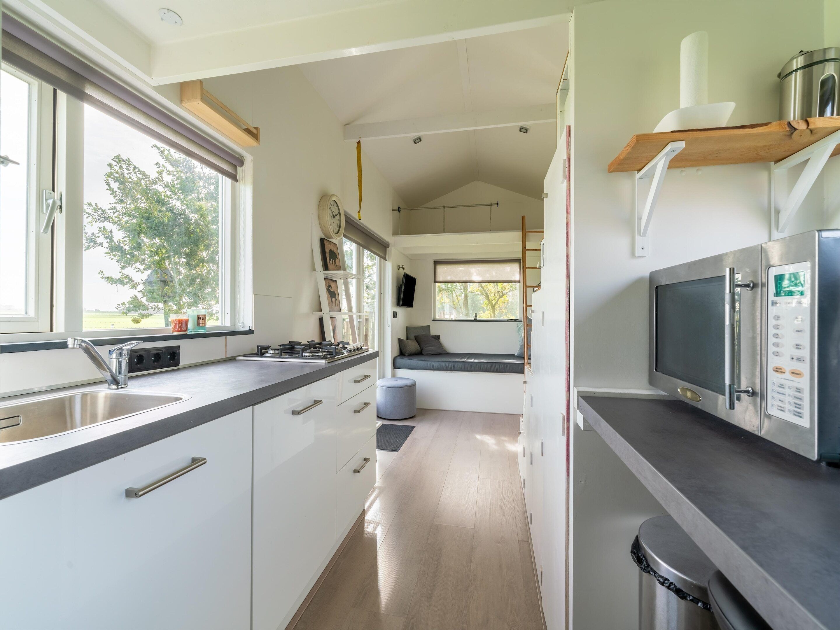 Una cocina moderna con estufa integrada, un lavamanos y un microondas. Hay una ventana con vistas a árboles y un banco con cojines.