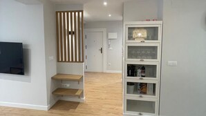 A modern living room with a flat-screen TV, wooden shelves, a glass cabinet with wine bottles, and a staircase leading to another room. - ¡Pisazo a estrenar en pleno centro! (Santander)
