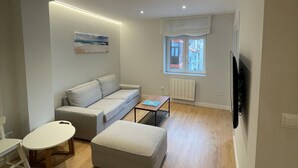 A modern living room with a sofa, a small table, a TV, and a window with a view of buildings. - ¡Pisazo a estrenar en pleno centro! (Santander)