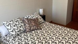 Un lit bien fait, avec une literie à motifs, une table de chevet avec une lampe et un mur sobre.