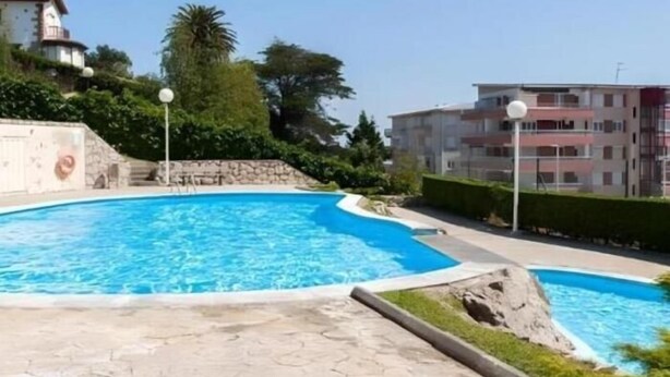 Une piscine dotée d’une plage en pierre, entourée de verdure et de bâtiments résidentiels.
