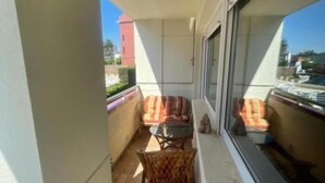 Un balcon avec deux fauteuils en osier et une petite table, d’où l’on peut admirer un bâtiment rouge et de la verdure.