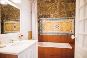 A bathroom with a white sink, a bathtub, and a stone wall. - Quinta De Guimaraes (Baiao)