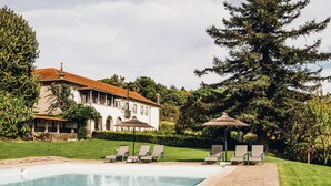 A pool area with lounge chairs and a building in the background. - Quinta De Guimaraes (Baiao)