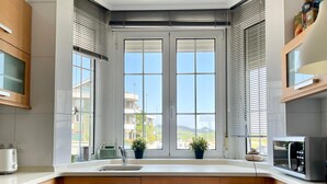 Une cuisine moderne dotée d’une grande fenêtre, de meubles en bois, d’un plan de travail blanc et d’un four à micro-ondes.