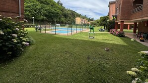 Una piscina envoltada per una tanca, amb una zona verda i un edifici al fons.