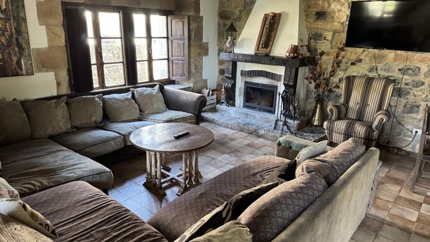 A cozy living room with a stone fireplace, a large sectional sofa, and a striped armchair. - Spectacular house in Castaneda (Castaneda)