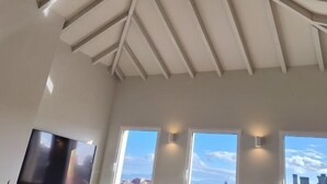 A room with a sloped ceiling, large windows, and a flat-screen TV.