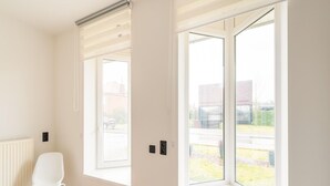 A room with a white radiator, a white chair, and two windows with blinds.