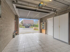 Un garage propre, carrelé, avec un plafond en béton, une grande porte blanche et une vue sur un immeuble moderne à l’extérieur.