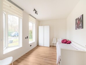 Une chambre à coucher comprenant un lit, une chaise, une armoire et une fenêtre avec des stores.