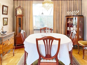 Uma sala de jantar com uma mesa redonda, cadeiras, um candelabro, um relógio e uma menora.