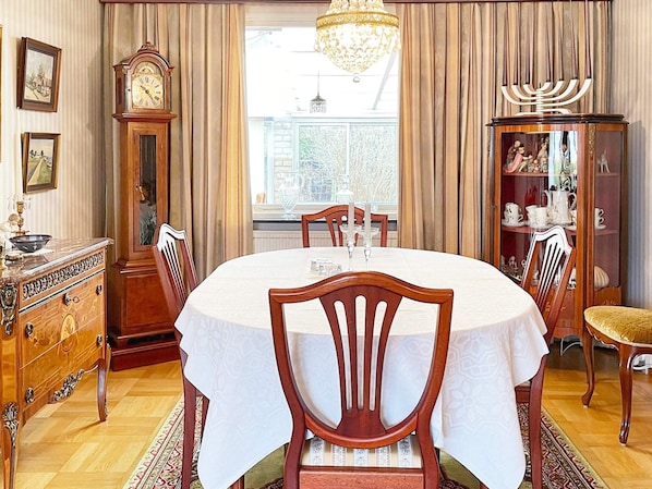A dining room with a round table, chairs, a chandelier, a clock, and a menorah.