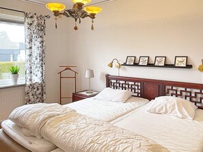 Quarto de hotel com cama, mesa de cabeceira, luminária, janela com cortinas e vista para o verde lá fora.