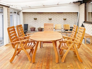 A round wooden table with eight chairs, a brick wall, and a glass door in the background.
