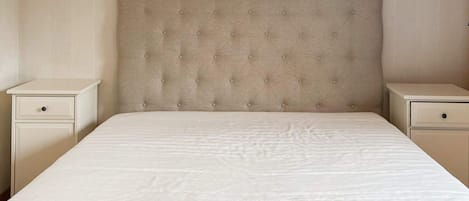 A bed with a tufted headboard, two bedside tables, and a plain wall.