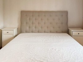 Un letto con testiera trapuntata, due comodini e una parete semplice.