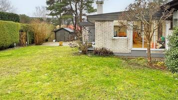En bostadsfastighet med en välskött gräsmatta, ett hus byggt av tegel och ett litet förråd.