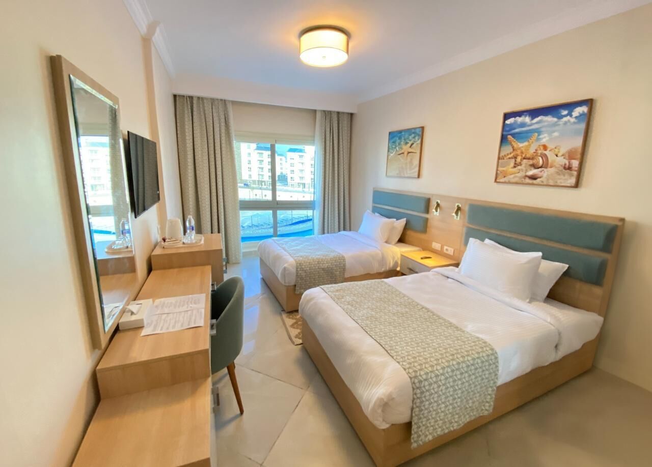 Une chambre d’hôtel avec deux lits, un bureau, une chaise et une grande fenêtre avec des rideaux.