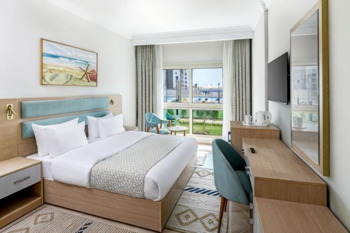 Una habitación de hotel con cama, escritorio, silla, televisor y balcón con vistas.