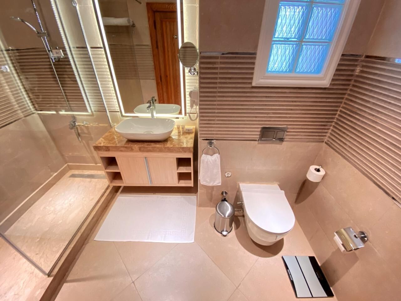 Une salle de bain moderne dotée d’une douche à parois de verre, d’un meuble-lavabo avec un évier, de toilettes et d’une fenêtre laissant entrer la lumière naturelle.