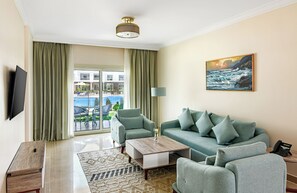 Sala de estar con sofá, sillones, mesa de centro, televisor de pantalla plana, un cuadro y vista a una piscina y zona exterior.