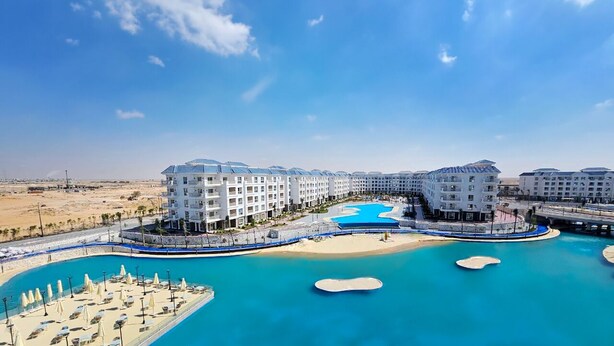 A resort with multiple buildings, a large central pool, and a beach area. - Azur One Eleven - New Alamein (El Alamein)