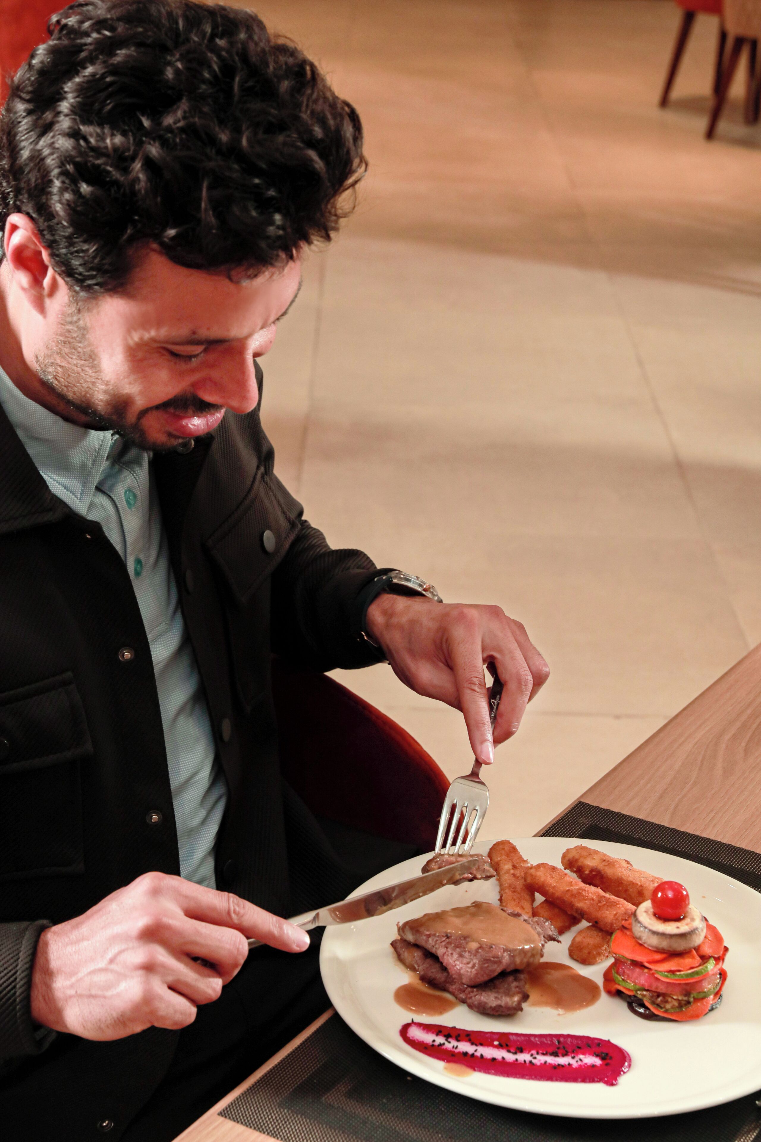 A person seated at a table with a plate of food, a fork, and a knife.