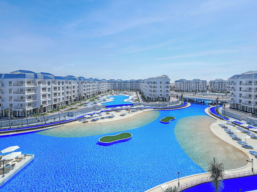 A resort with a large swimming pool, multiple buildings, and a beach area.