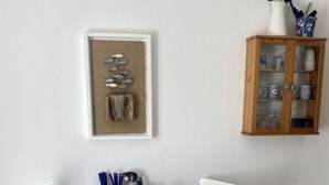 A dining area with a wooden table and white chairs, a framed artwork above the table, and a cabinet with kitchenware.