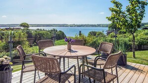 Une table ronde d’extérieur, entourée de chaises en osier, avec une plante en pot et une vue sur un lac.