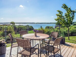 A round outdoor table with wicker chairs, a potted plant, and a view of a lake. - 5 Star Holiday Home in Kolding (Kolding)