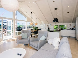 A modern living room with a sofa, armchairs, a dining area, and a kitchen with a large window. - 5 Star Holiday Home in Kolding (Kolding)