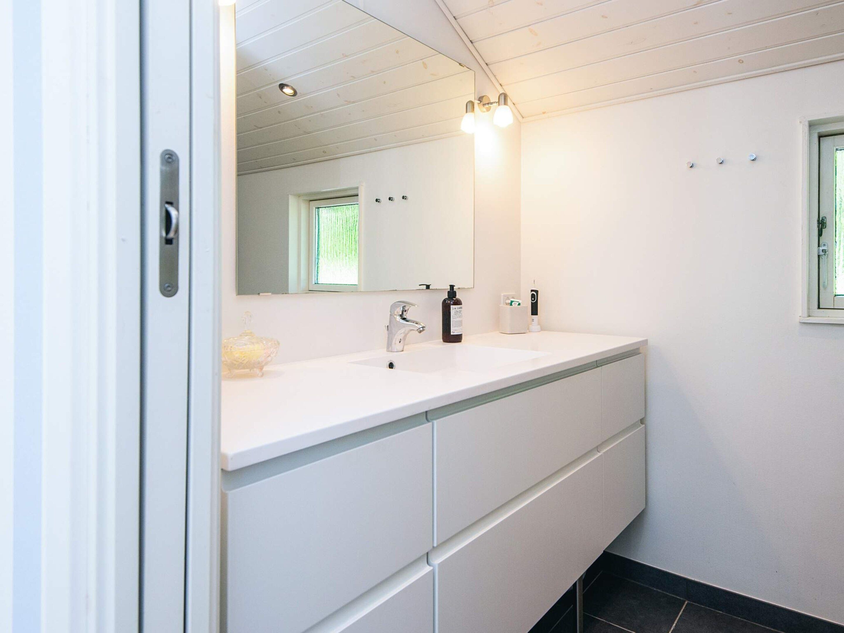 A bathroom with a white vanity, a mirror, a window, and a sink.