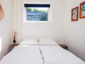 A bedroom with a bed, a window, a wall-mounted picture, and a bedside table with a vase. - 5 Star Holiday Home in Kolding (Kolding)