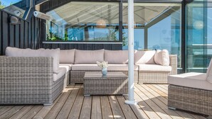 Un espace extérieur moderne, aménagé avec des meubles en osier, une structure vitrée et offrant une vue sur l’extérieur.