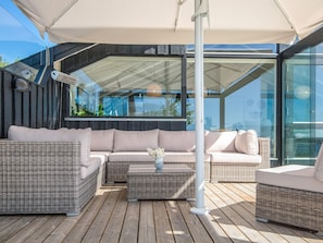 A modern outdoor seating area with wicker furniture, a glass enclosure, and a view of the outdoors. - 5 Star Holiday Home in Kolding (Kolding)