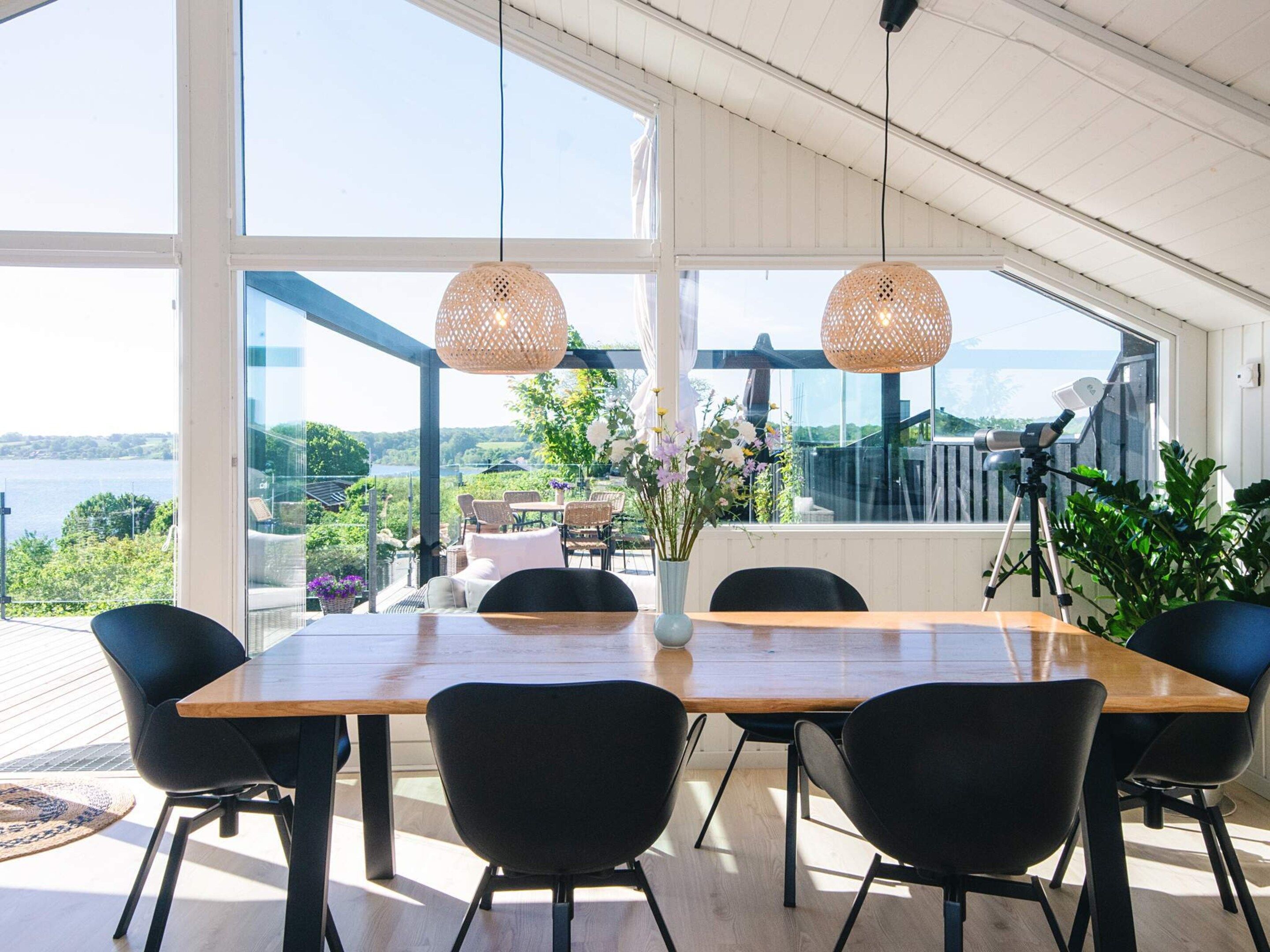 A dining area with a wooden table and black chairs, large windows offering a view of the outdoors, and a telescope on a balcony.
